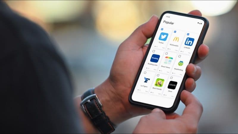 Человек, держащий мобильный телефон с девятью приложениями на экране